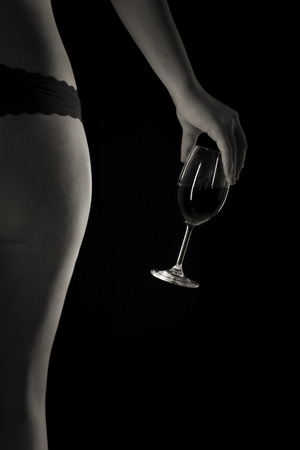 Erotic partial view of the legs of the back and buttocks of a young woman casually holding a glass of red wineの写真素材