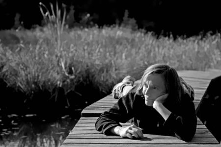 Woman relaxes on one of the last autumn days and lies on the landing stage of a small moor lakeの写真素材