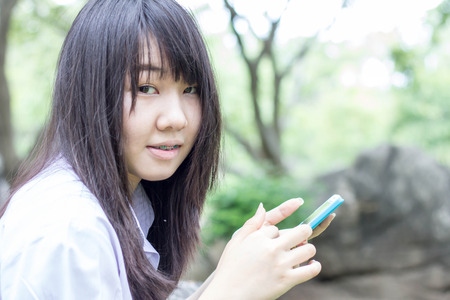 Portrait of thai student teen beautiful girl using her smart phone sitting in park.の写真素材