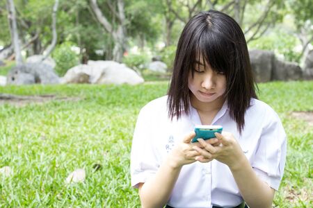 Portrait of thai student teen beautiful girl using her tablet sitting in park.の写真素材