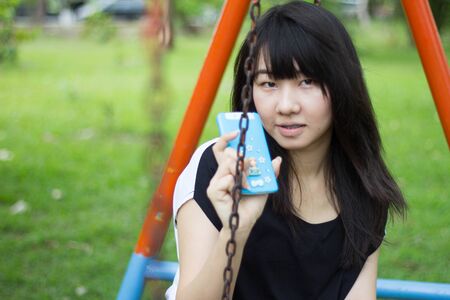 Portrait of thai student teen beautiful girl using her smart phone sitting in park.の写真素材