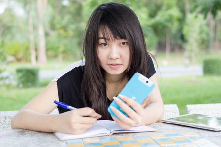 Portrait of thai student teen beautiful girl using her smart phone sitting in park.の写真素材