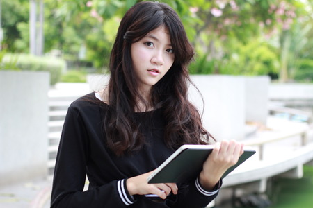 Portrait of thai student teen beautiful girl using her tablet sitting in park.の写真素材
