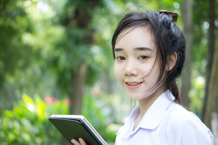 Portrait of thai student teen beautiful girl using her tablet sitting in park.の写真素材