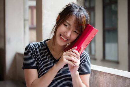 Portrait of thai adult student university uniform beautiful girl reading red bookの写真素材