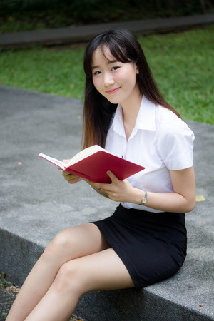 Portrait of thai adult student university uniform beautiful girl read red bookの写真素材