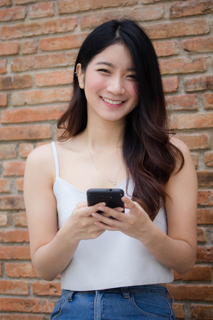 Portrait of thai china adult beautiful girl White shirt blue jeans using her smart phoneの写真素材