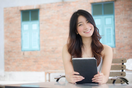 Portrait of thai china adult beautiful girl White shirt blue jeans using her tablet.の写真素材