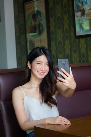 Portrait of thai china adult beautiful girl White shirt blue jeans using her smart phone Selfie