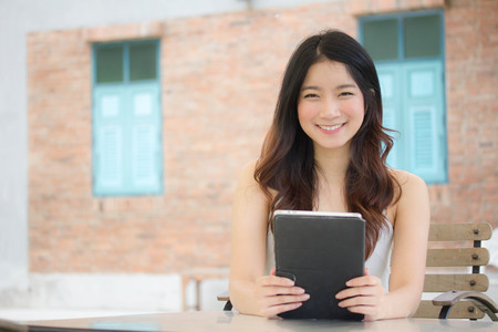 Portrait of thai china adult beautiful girl White shirt blue jeans using her tablet.
