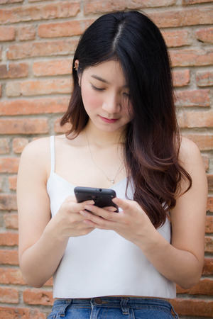 Portrait of thai china adult beautiful girl White shirt blue jeans using her smart phoneの写真素材