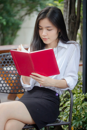 Portrait of thai adult working women white shirt reading red bookの写真素材