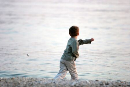 Boy throwing stones into the seaの写真素材