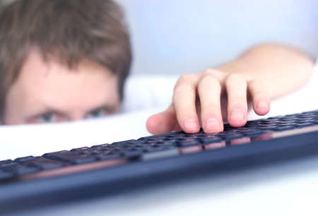 Man peeks over the edge of a desk with hand on keyboard;の写真素材