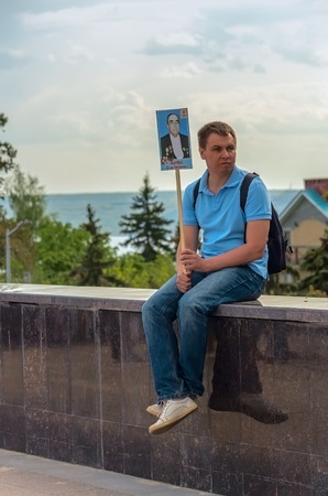ULYANOVSK, RUSSIA - MAY 9, 2016: ULYANOVSK, RUSSIA - MAY 9, 2016: A young man with a portrait of a veteran of World War II monument sits on the fence after taking part in the procession of the Immortal regiment. May, 9, 2016 in Ulyanovsk city, Russia.のeditorial素材