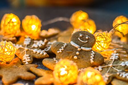Smiling gingerbread man lies among cookies and rattan New Year garlands on the festive table.