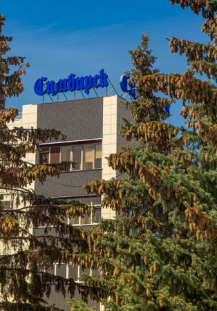 Russia, Ulyanovsk, May, 9, 2023: The logo of the Simbirsk business center is against the sky. In the foreground of the top of the fir trees.のeditorial素材