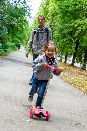 Grandfather and granddaughter riding scooters in the park on a sunny day.の写真素材