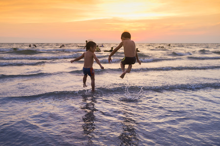 silhouette two boys are playing in the sea during a sunsetの写真素材