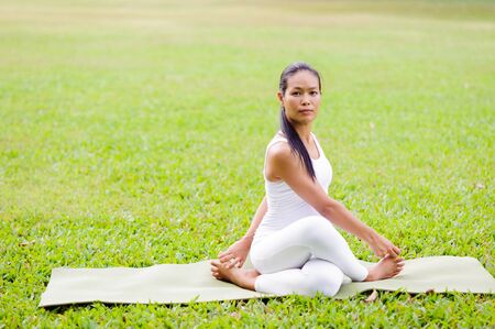Beautiful woman practicing yoga twist pose in the park.