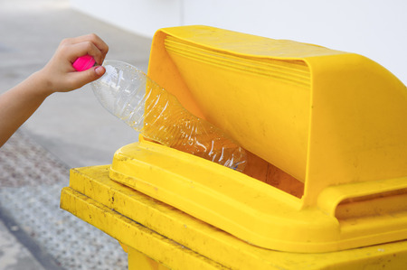 Children hand dropping used bottle in the yellow trash