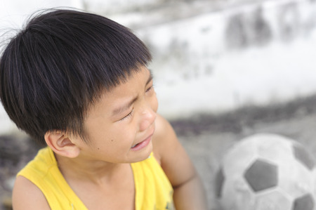 Young boy cry and tear during play football in front of concrete wall of concrete wallの写真素材
