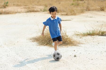 Boy play football on the dry soil ground in a shiny day