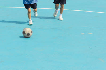 Boy play football on the blue floor in a shiny dayの写真素材