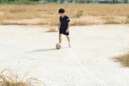 Out focus boy play football on dry soil ground in a shiny dayの写真素材