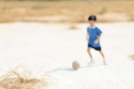 Out focus boy play football on dry soil ground in a shiny dayの写真素材
