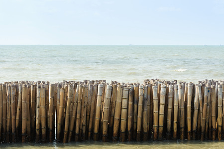 Old bamboo fence on the sea preventing the wave under blue sky and cloudの写真素材