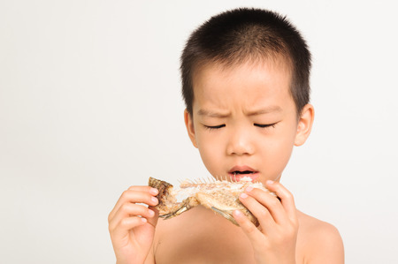 Young asian boy eating fish showing bone on white backgroundの写真素材