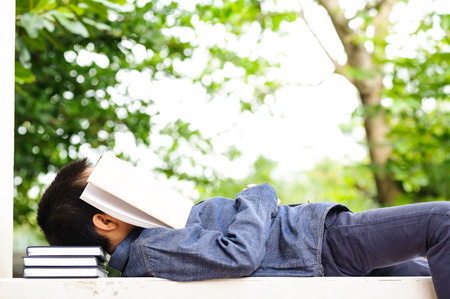 Young boy sleeping with books in the gardenの写真素材