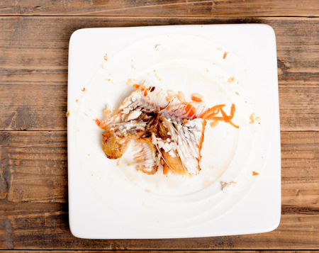 Fry fish bone after finish eating on white plate on wood tableの写真素材