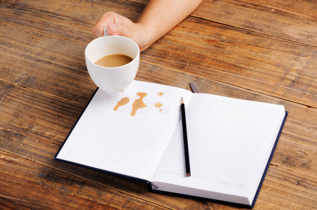 Coffee in cup drop on the white page notebook and pencilの写真素材