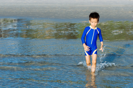 Boy in blue swim suit run in on the beach and seaの写真素材
