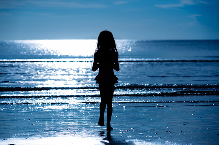 Blue tone Silhouette style little girl on the beach during golden sunlightの写真素材