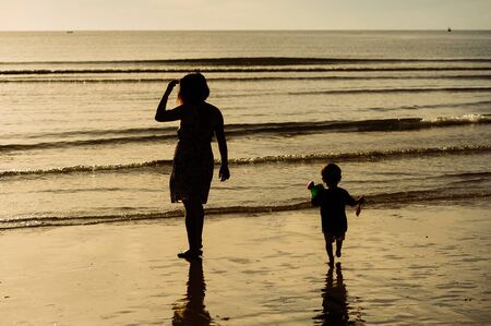 Silhouette mother and child on the beach during sunlightの写真素材