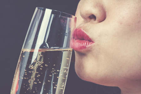 Vintage tone Close up focus on red lip Asian young woman kiss champagne on black backgroundの写真素材