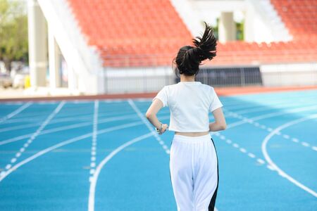 Young woman jogging on the blue track in the stadium during the day