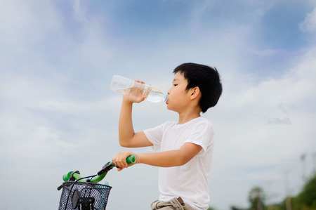 Asian young boy sit on bicycle  drinking fresh water from plastic bottle after sport in daylightの写真素材