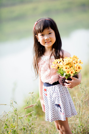 Portrait little cute Asian girl in the beautiful dress on weed grass field beside road and mountain backgroundの写真素材