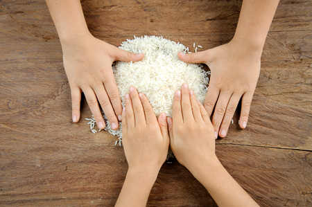 Close up child hand pour Thai rice grain on wood tableの写真素材