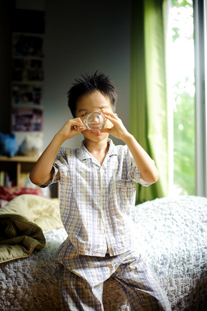 Close up young asian boy drink water from transparent glass after wake up in the morning from the bedの写真素材