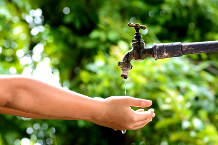 Close up kid hand wait for water drop from old grunge brass faucet on green bokeh from tree...