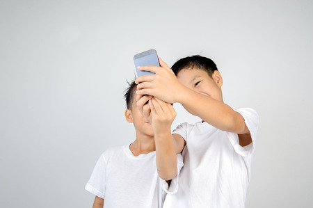 Two asian white shirt boy use smartphone for selfie together. On white background.の写真素材