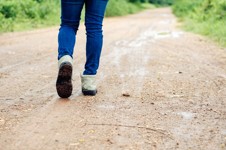 Dak color tone. Woman traveller in boot walk on the wet dirty road in urban forest.の写真素材