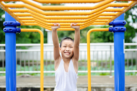 Young asian boy hang the yellow bar by his hand to exercise at out door playground