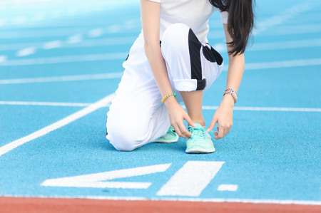 Young woman prepare her shoe before running on number four blue track
