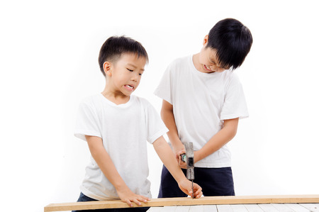Asian older brother do not careful and close his eye and use hammber to hit the nail that his brother holding.の写真素材